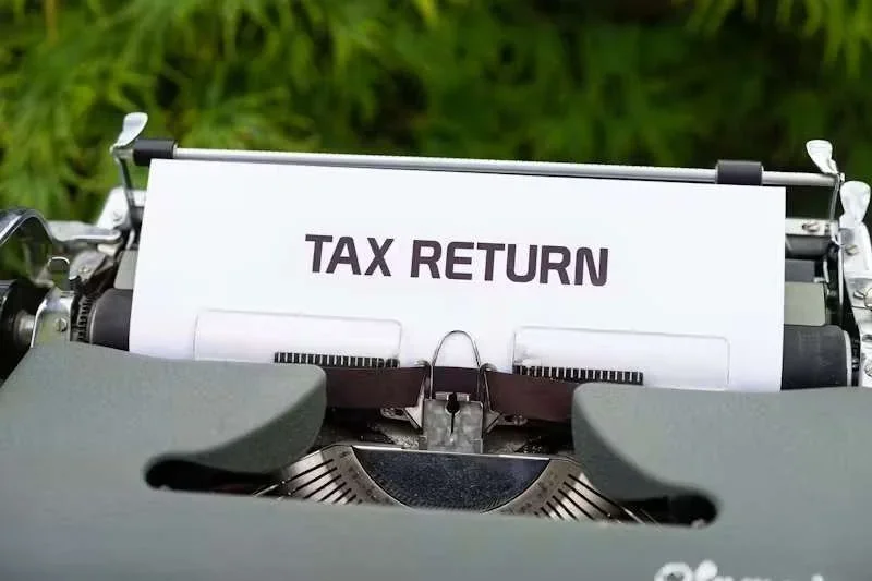Máquina de escrever antiga com papel branco, escrito 'TAX RETURN', e fundo verde desfocado