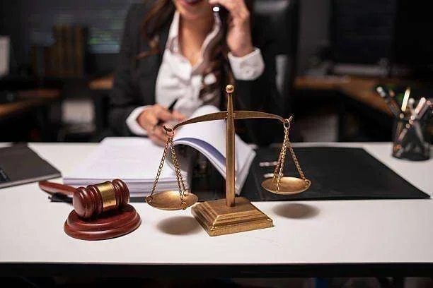 Martelo de juiz, balança da justiça e documentos em mesa de escritório com advogado ao telefone